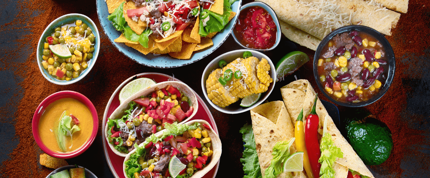 mexican meal board with tacos, nachos, guacamole, salsa and fresh veggies on a dark background