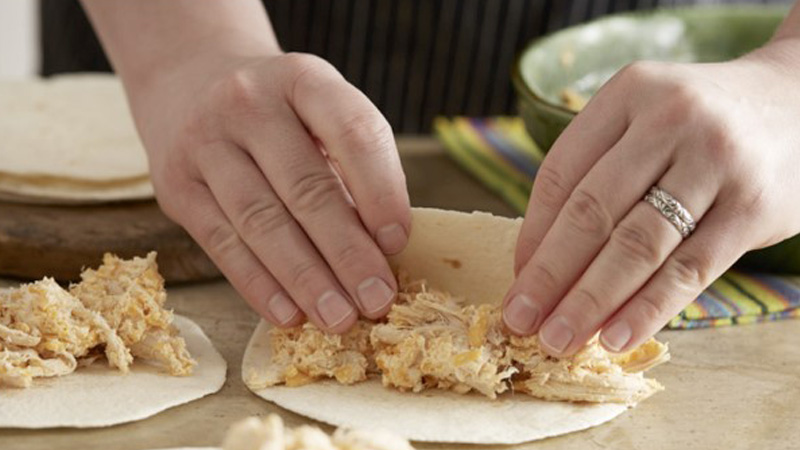 a person rolling tortillas filled with meat