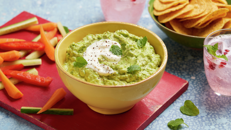 Minted Pea Guacamole served in a bowl on a red wooden board