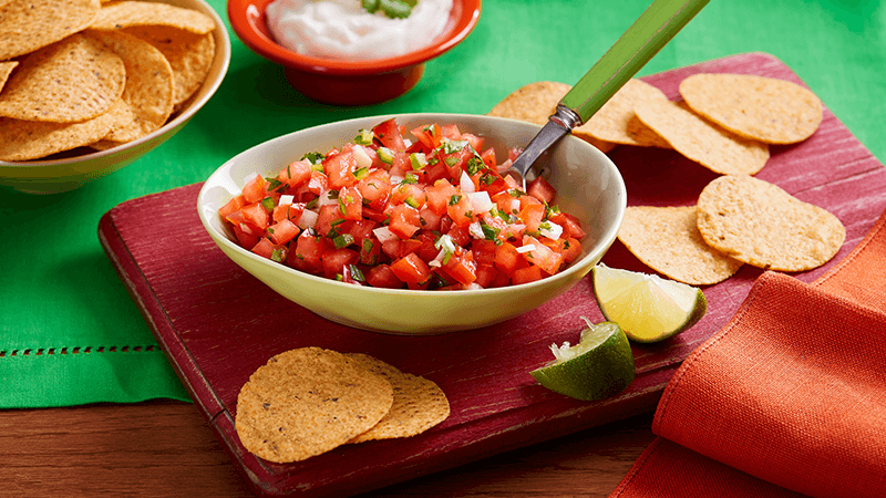 Nachips with homemade salsa served in a white bowl with a spoon placed on a red board